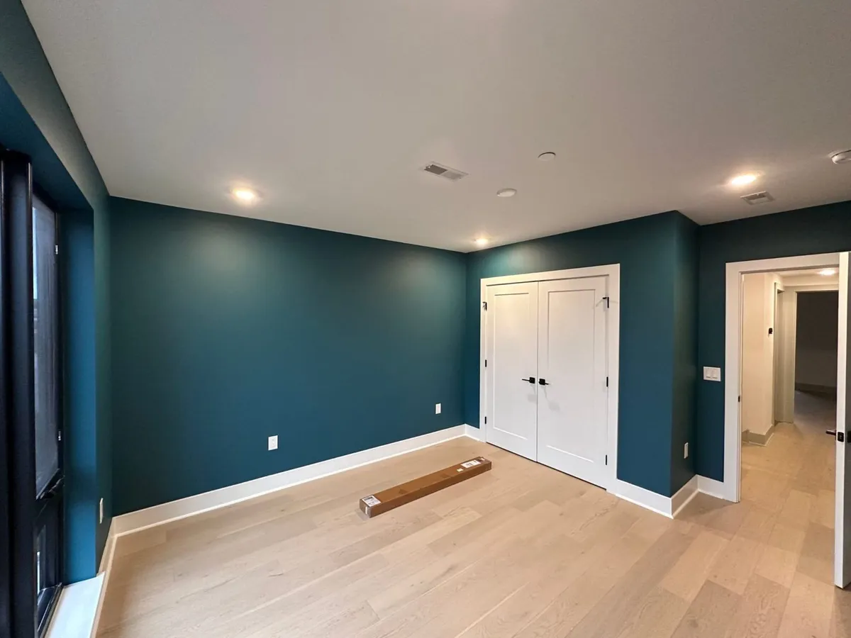 Finished bedroom painted deep teal-blue with crisp white trim and light wood floors in Satellite Beach, FL